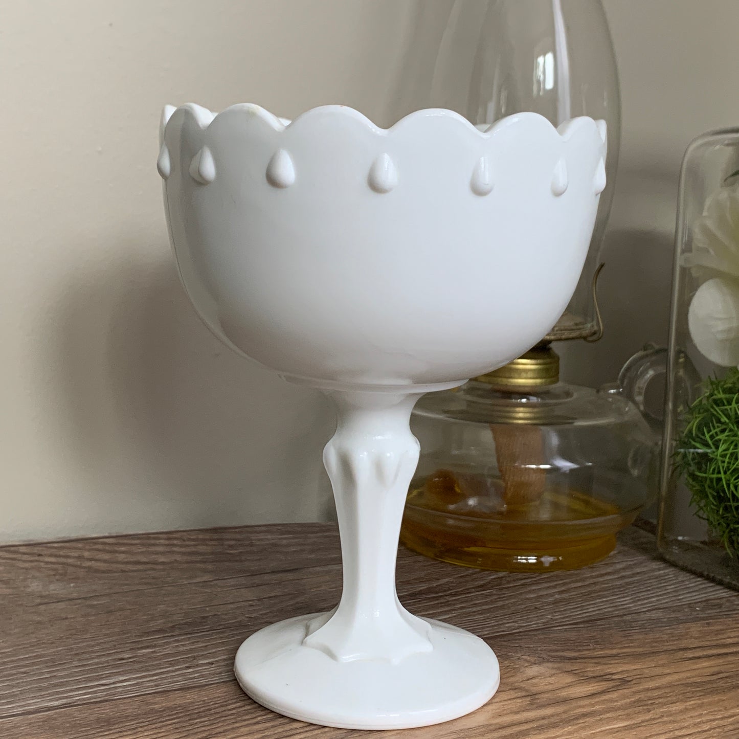 A footed milk glass dish with a scalloped rim and a raised teardrop pattern