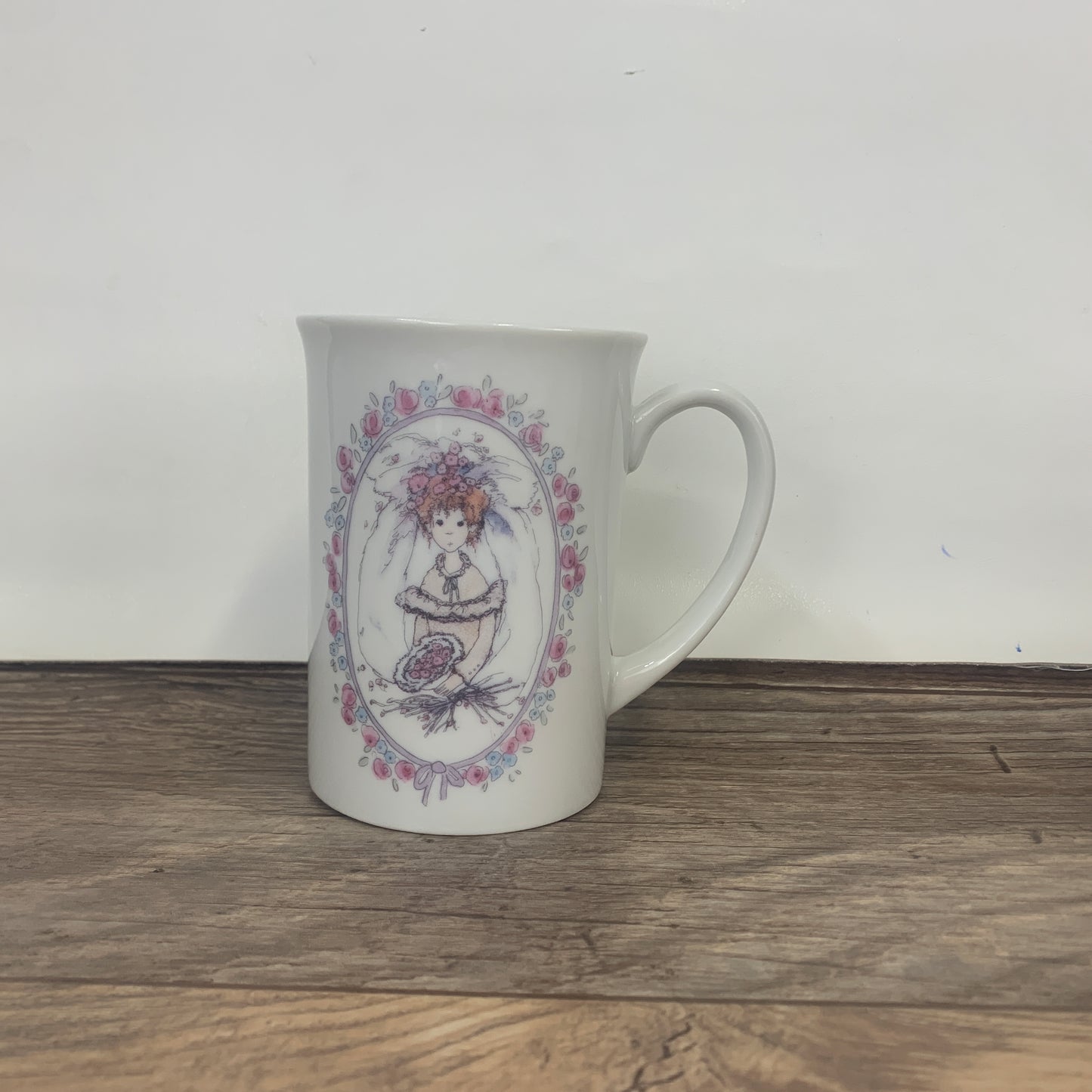 A tall ceramic mug decorated with a bride in a floral frame