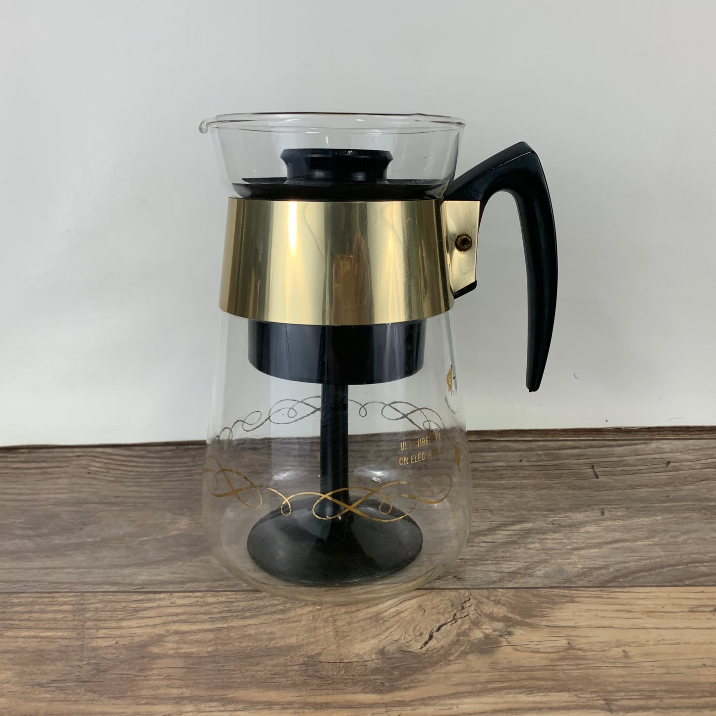 A glass coffee percolator with a wide gold band and black plastic insert
