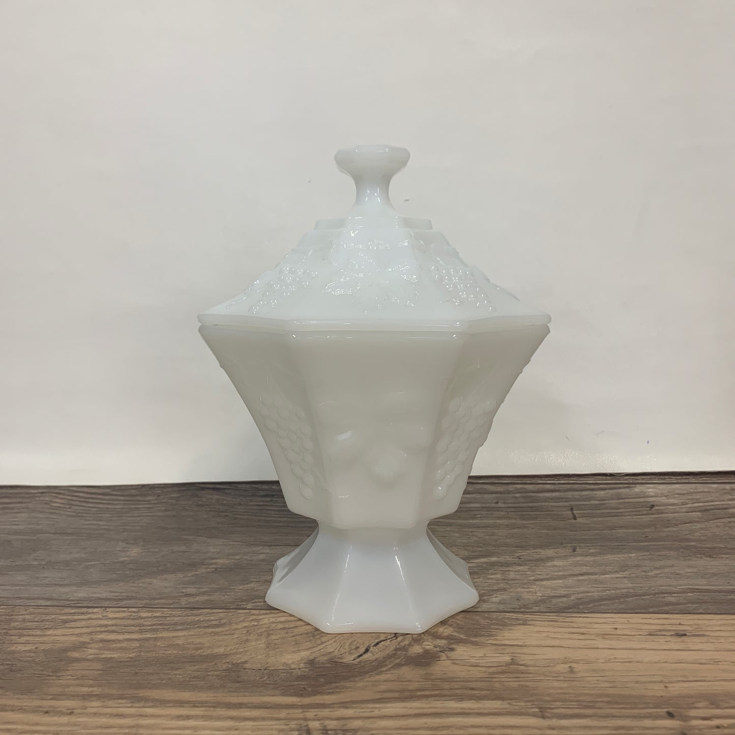 A white octagon shaped candy dish with a raised grape leaf pattern and lid