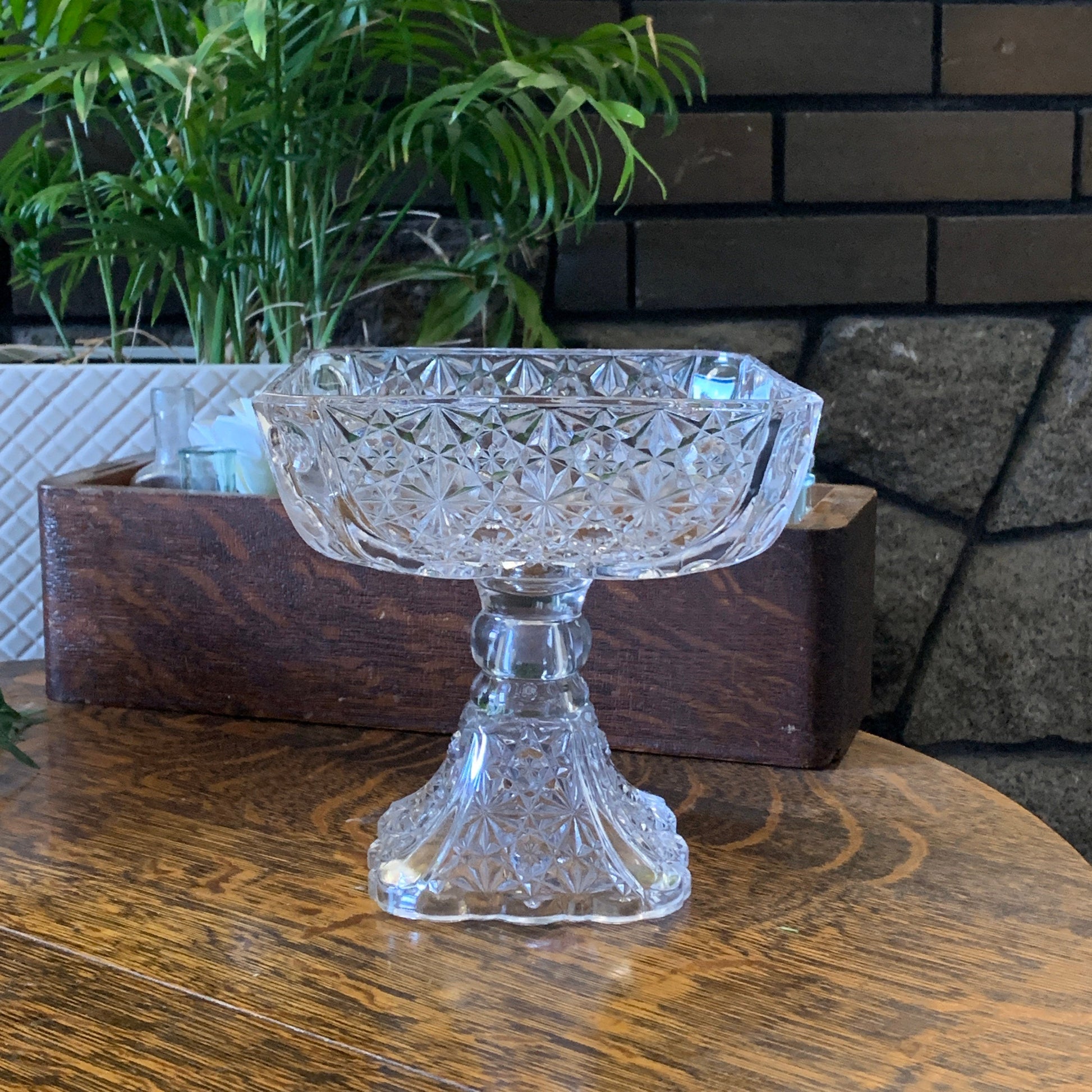 A tall square dish on a raised pedestal with a daisy and button pressed pattern