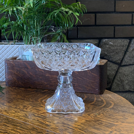 A tall square dish on a raised pedestal with a daisy and button pressed pattern