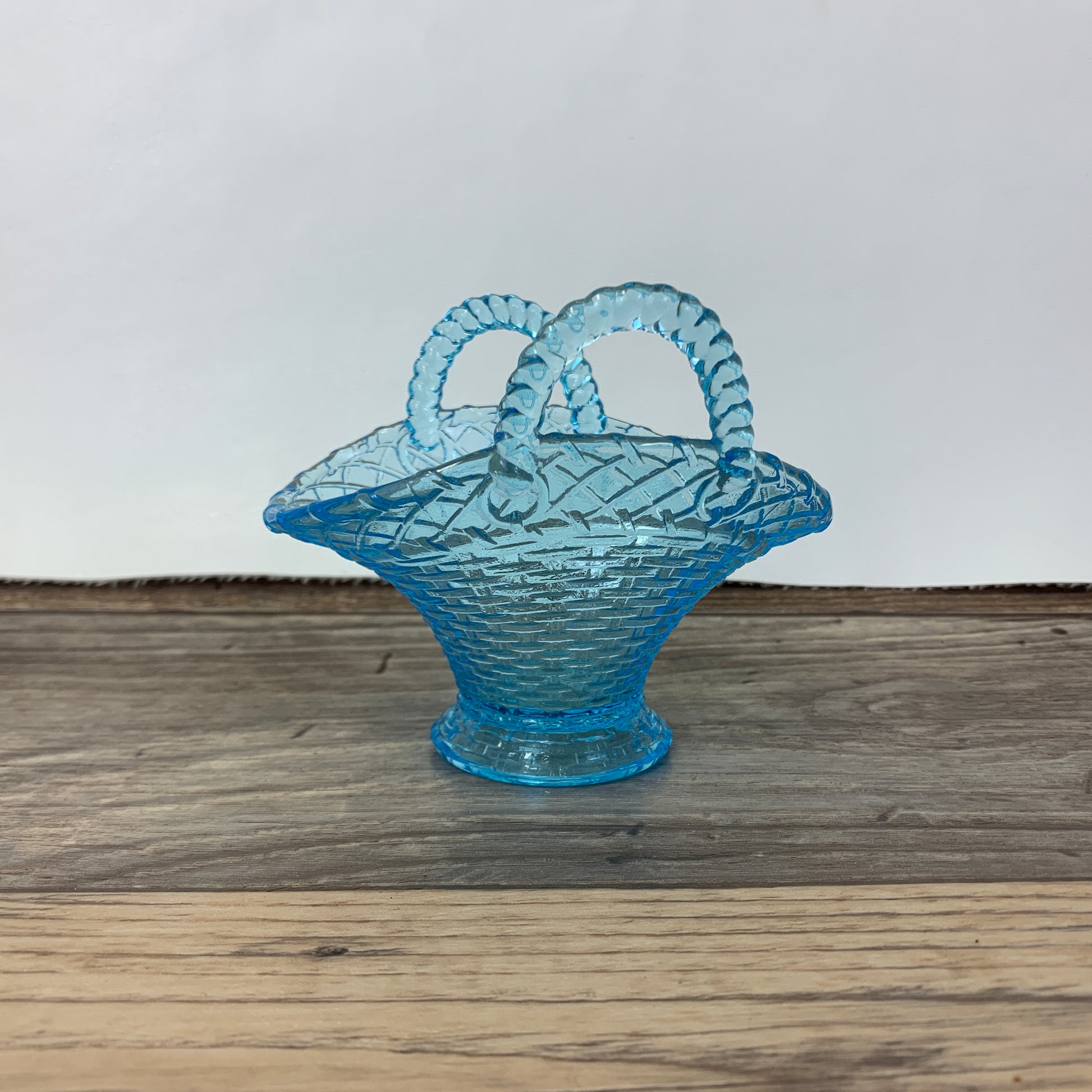 A small light blue glass basket with two handles and a basket weave pattern