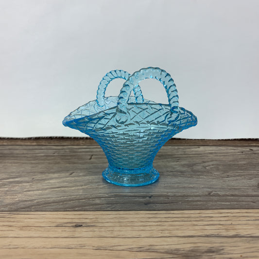 A small light blue glass basket with two handles and a basket weave pattern