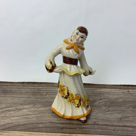 A dancing girl in Eastern European traditional clothing. A cream coloured dress with orange highlights.