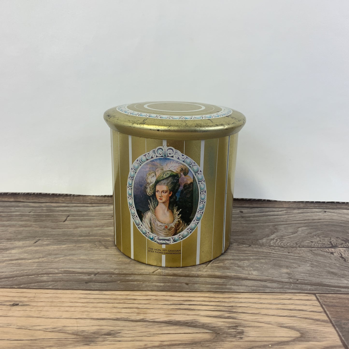 A tall gold tin with Thomas Gainsborough paintings on the side.