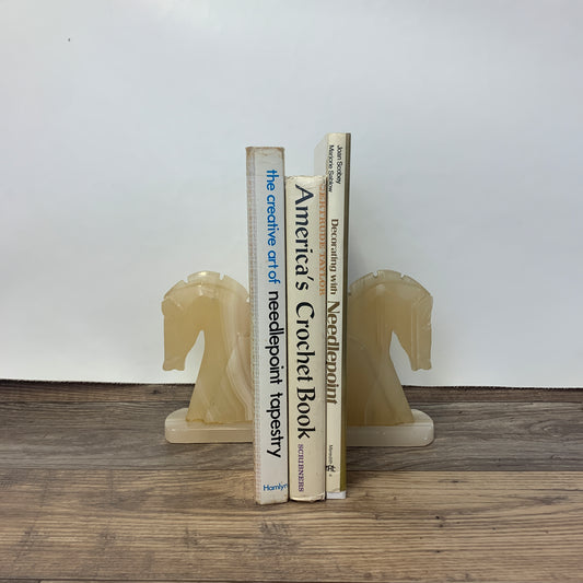 A set of two horse head bookends holding several books between them.