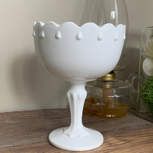 A footed milk glass dish with a scalloped rim and a raised teardrop pattern