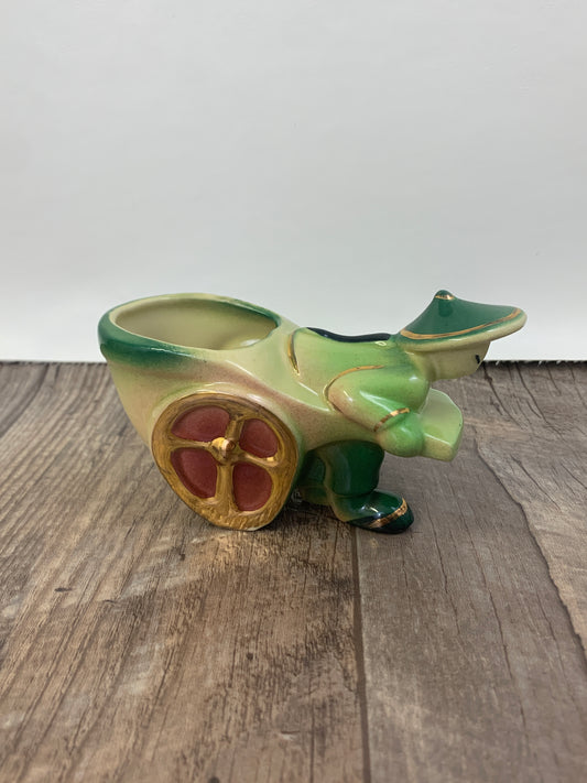 A small green planter with gold trim of a person wearing traditional dress pulling a small cart.