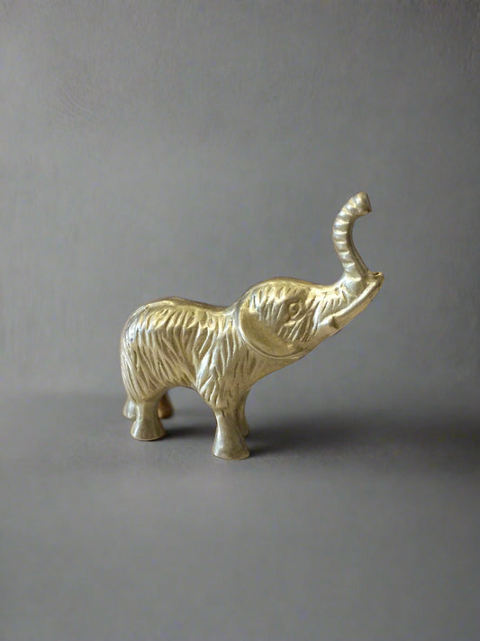 A small brass figurine of an elephant with its trunk raised, placed on a flat surface.