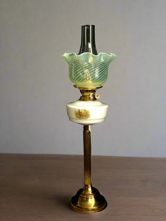 A tall oil lamp with a brass coloured foot, milk glass font, and a swirl pattern shade