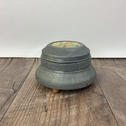 A metal jar with wooden feet and a porcelain insert on the lid