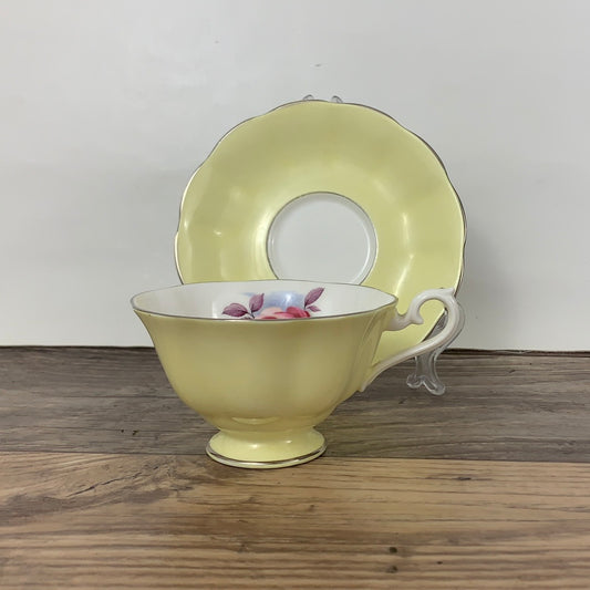 A bright yellow teacup trimmed in gold with a matching saucer standing behind it.